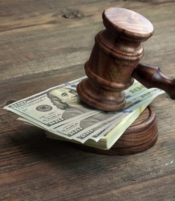 A stack of hundred-dollar bills underneath a wooden gavel on a desk