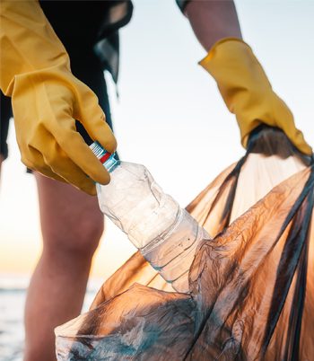 A person wearing yellow gloves putting a plastic bottle in a garbage bag
